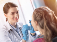 Woman doctor in white coat examining throat of sick little girl